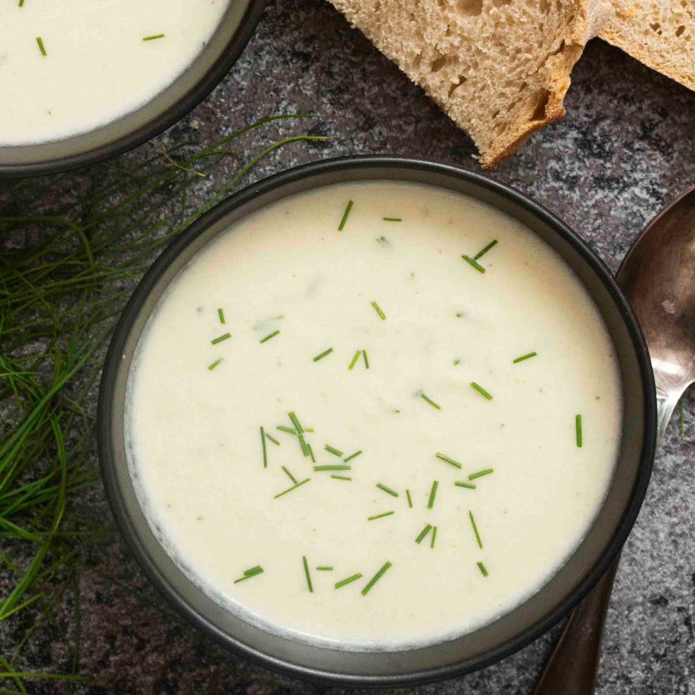 Black bowl filled with French Cauliflower & Andouille Soup with served with bread.